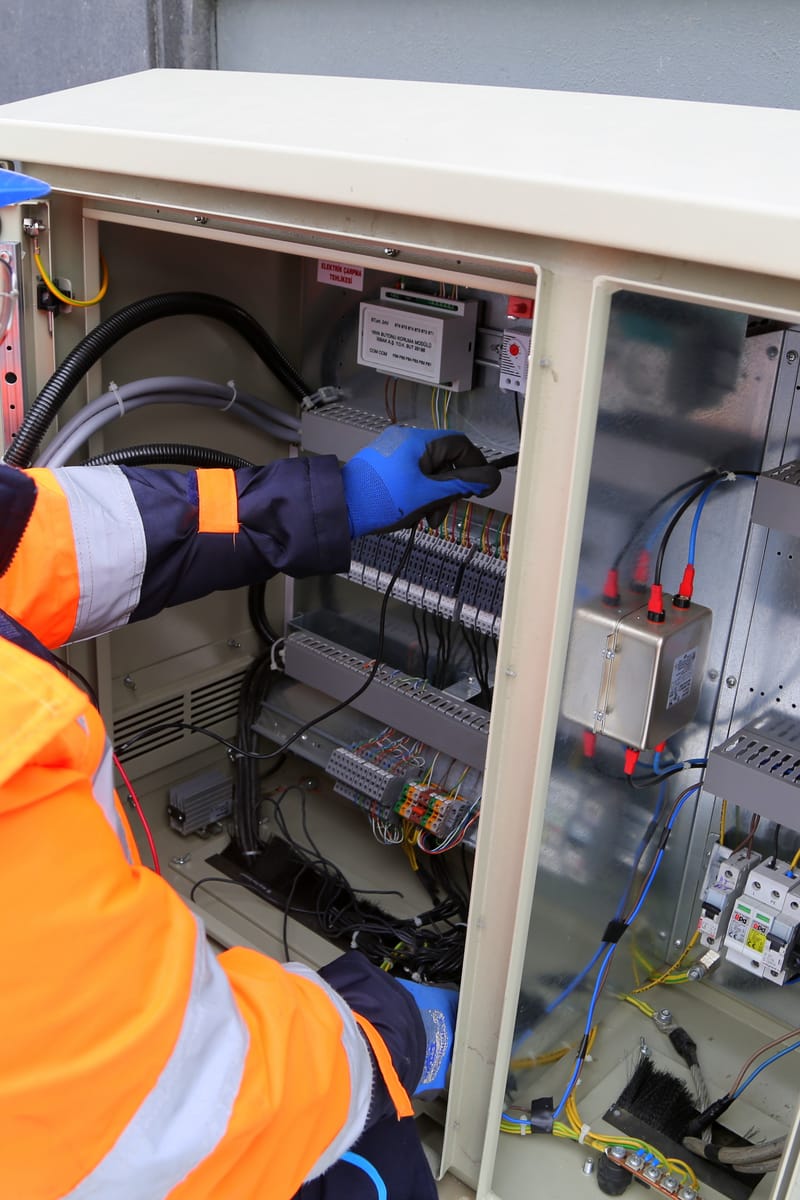 Engineer in safety gear working on an outdoor electrical panel, ensuring system functionality.